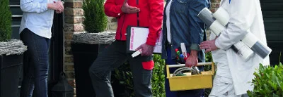 Drei Personen mit Werkzeug vor einem Haus